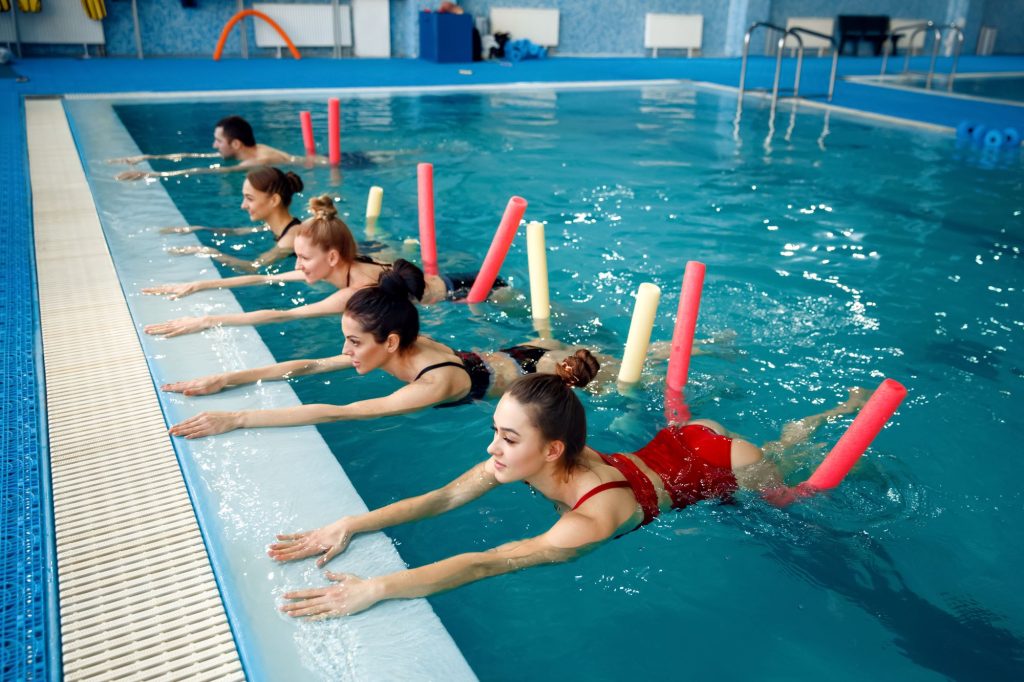 Você sabe quais são os benefícios da hidroginástica? Esse exercício de baixo impacto é indicado para todas as idades, inclusive para quem quer emagrecer, e traz diversas vantagens para a saúde.
Continue lendo este conteúdo e confira como a hidroginástica pode te ajudar.
O que é a hidroginástica?
A hidroginástica é um exercício aeróbico realizado dentro d’água com o auxílio de equipamentos de musculação ou natação.
As atividades são realizadas em piscina aquecida com temperatura da água entre 29ºC e 32ºC para relaxar os músculos e proporcionar conforto ao aluno. 
A intensidade pode variar de acordo com o objetivo de cada um, mas de forma geral, as aulas se iniciam com o aquecimento para elevar os batimentos cardíacos, partindo para exercícios que promovem resistência e o fortalecimento dos músculos e, no final para desacelerar, é realizado uma atividade de relaxamento