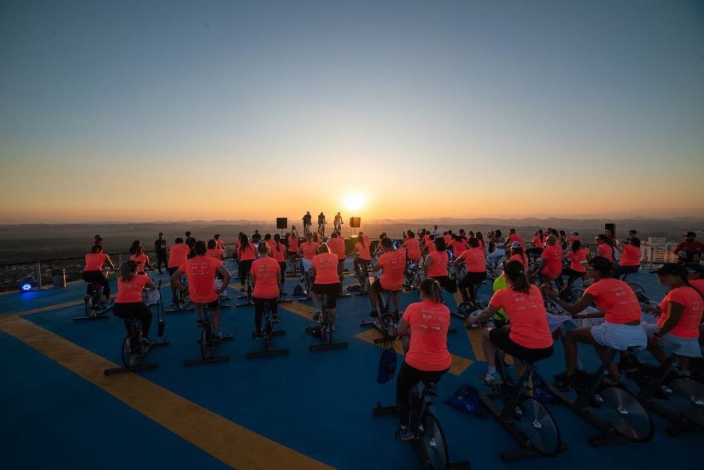 grupo de pessoas participando de uma aula de spinning ao ar livre durante o pôr do sol.