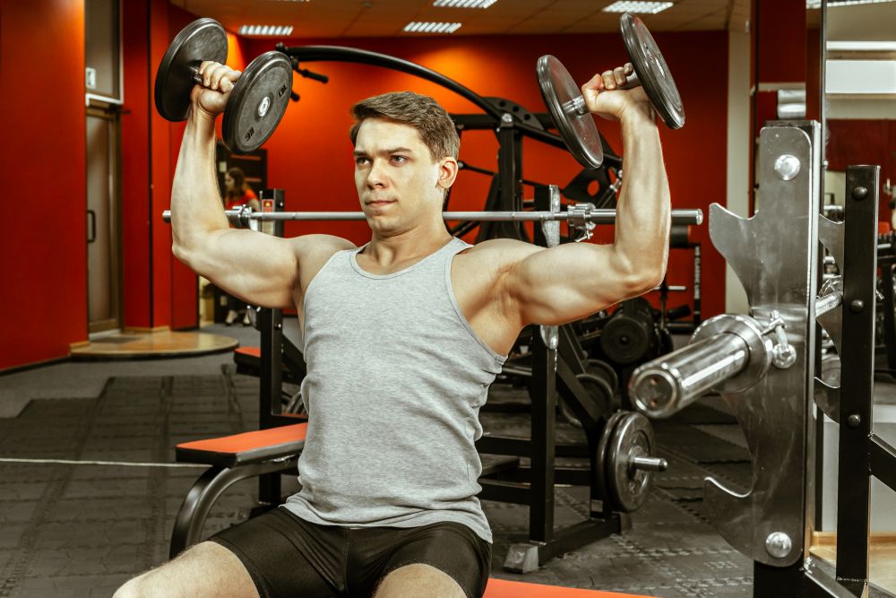 Homem fazendo desenvolvimento com halteres como exercícios para ombro.