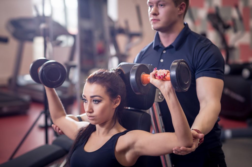 Mulher fazendo exercícios para ombro com ajuda do treinador.