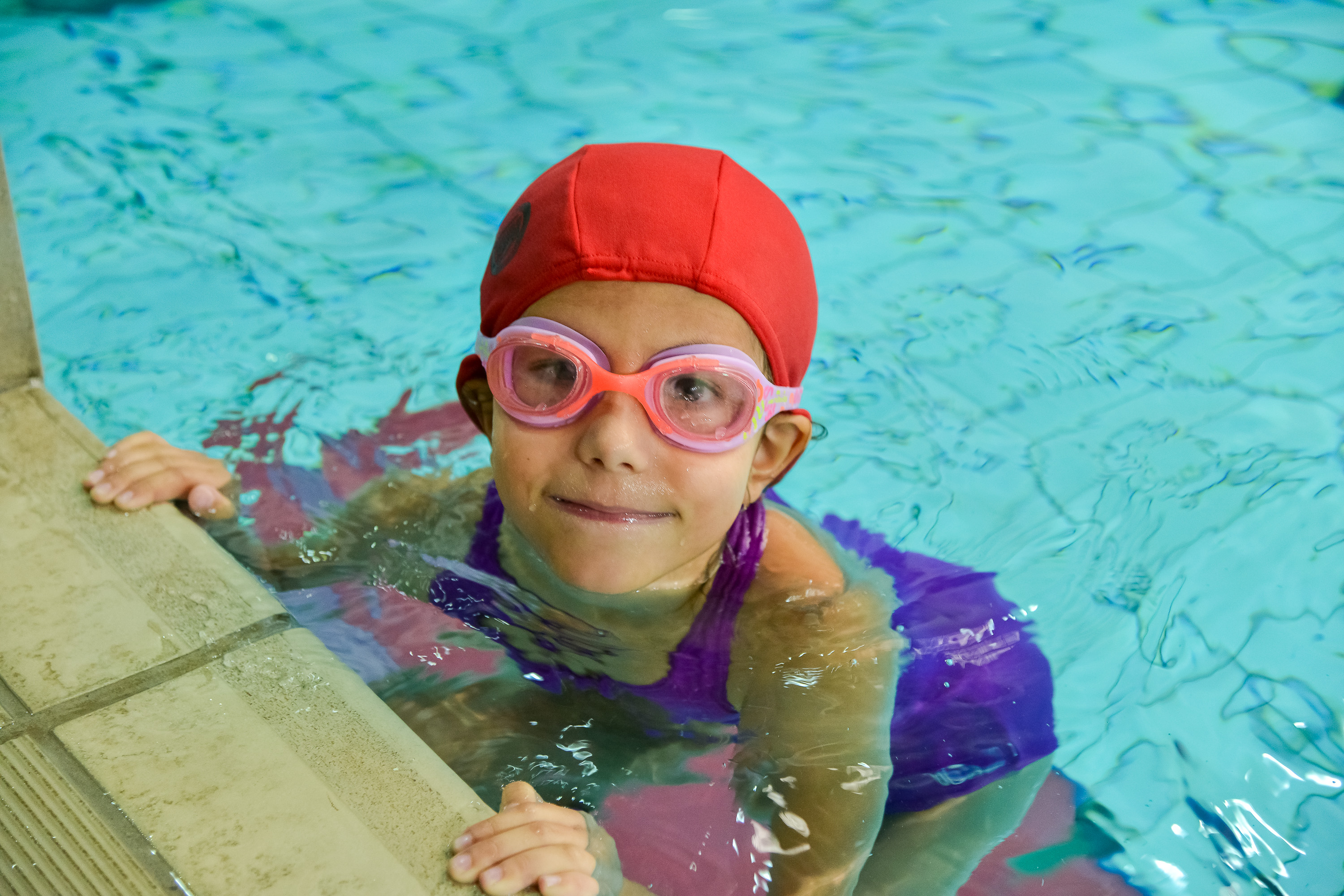 Criança usando touca e óculos de natação em piscina durante aula infantil.