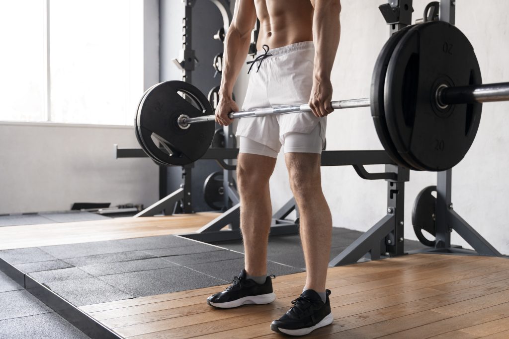 Homem levanta barra com pesos em treino de musculação na academia