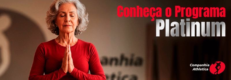 Mulher idosa de cabelos grisalhos, usando blusa vermelha, faz pose de meditação com as mãos unidas em frente ao peito. Ao lado, aparece o texto “Conheça o Programa Platinum”. No canto inferior direito está o logo da Companhia Athletica. A imagem promove atividades para idosos com foco em saúde, bem-estar e qualidade de vida.
